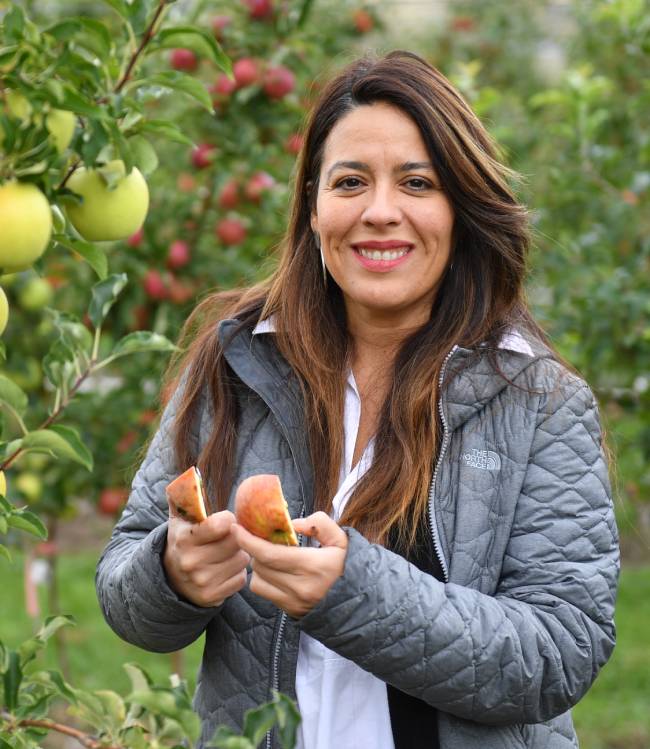 Carolina Torres standing in apple orchard holding cut apple.