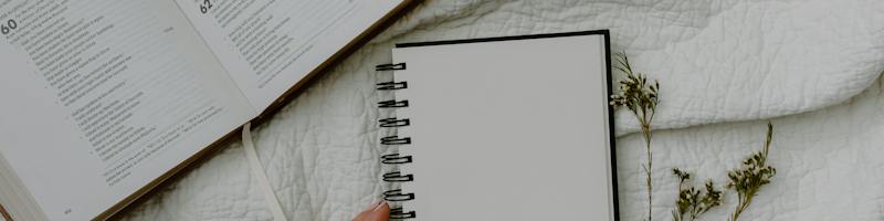 Person Holding White Spiral Notebook on White Fabric
