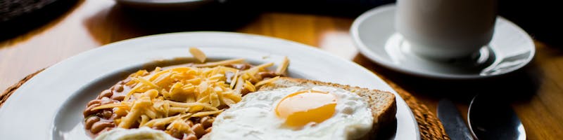 A hearty breakfast with fried eggs, baked beans, and toast served with coffee in a cozy setting.