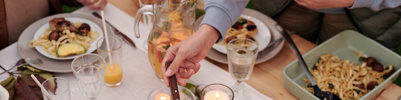 High angle of unrecognizable group of people eating together dinner with various dishes and drinks at table decorated with candles