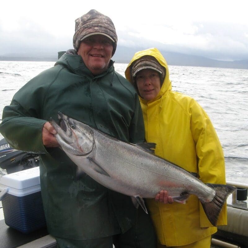 Elderly man and women stand on a fishing boat holding a salmon
