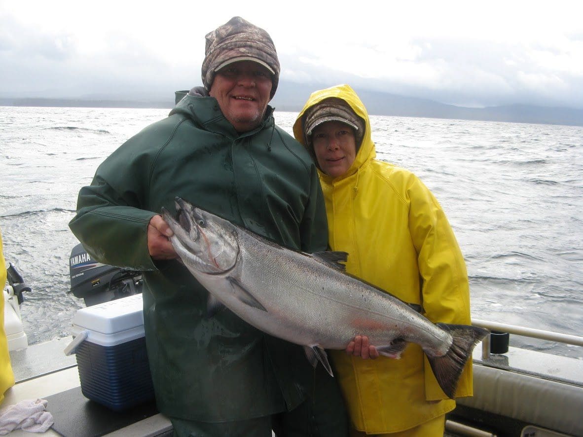 Elderly man and women stand on a fishing boat holding a salmon