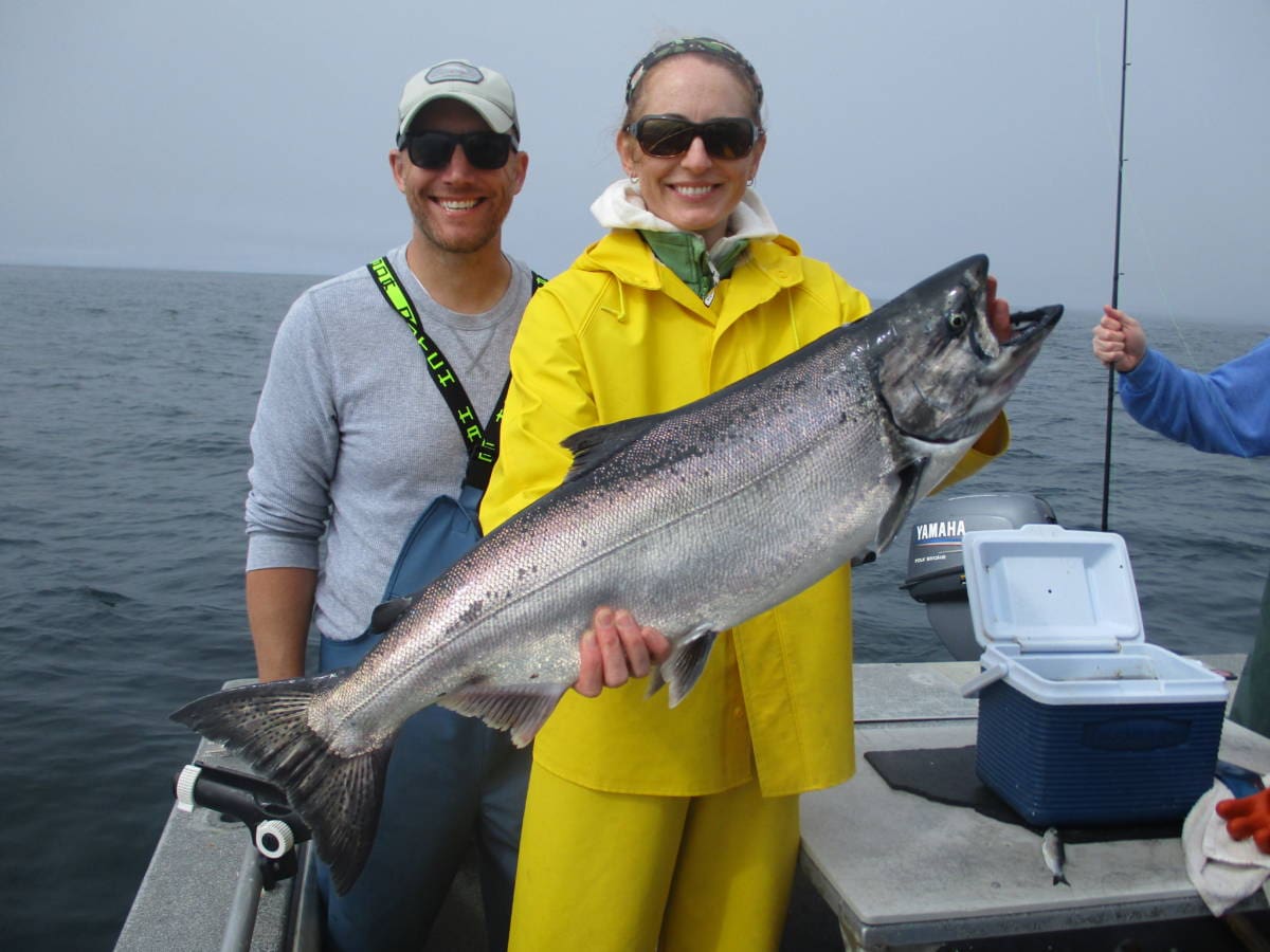 woman in yellow slickers holding large king salmon on boat