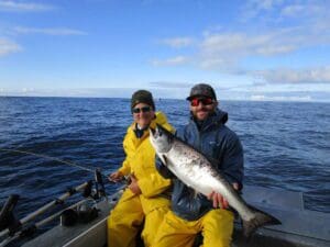 Gary and Kevin Rieschel 1 man holding salmon next to 1 man fishing on boat