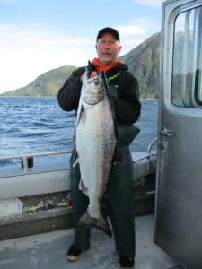 man in hat holding large king salmon on boar