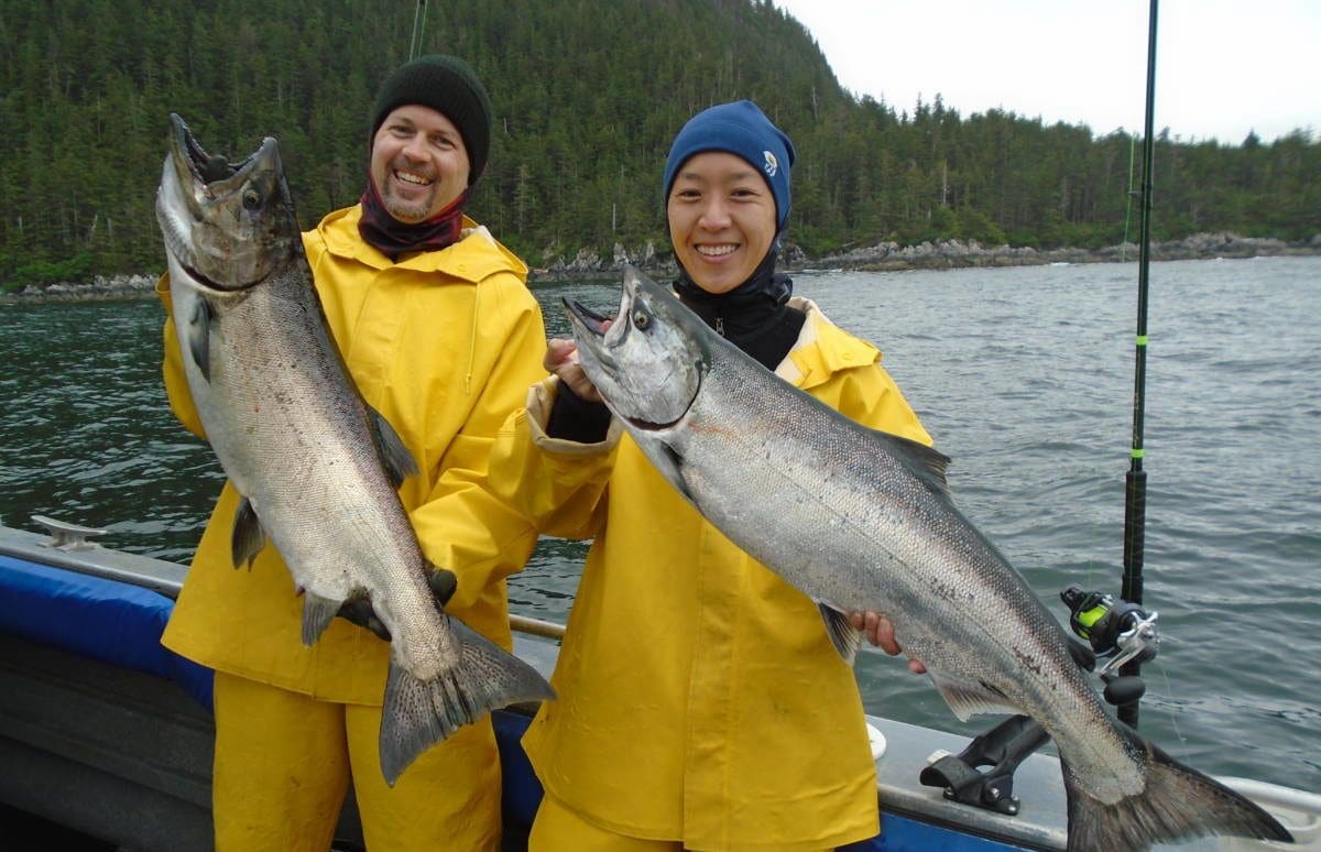 2 people in yellow slickers and hats holding large king salmon