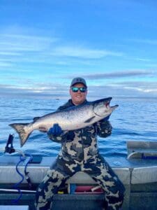 Chad Christopher image man sitting on boat in camo outfit holding salmon