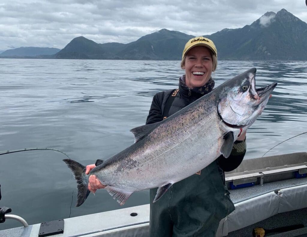 Carly-Pluskwick Woman smiles as she holds a large Alaskan King Salmon