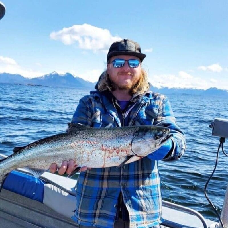 Man in sunglasses holds a salmon on a boat in Sitka, Alaska