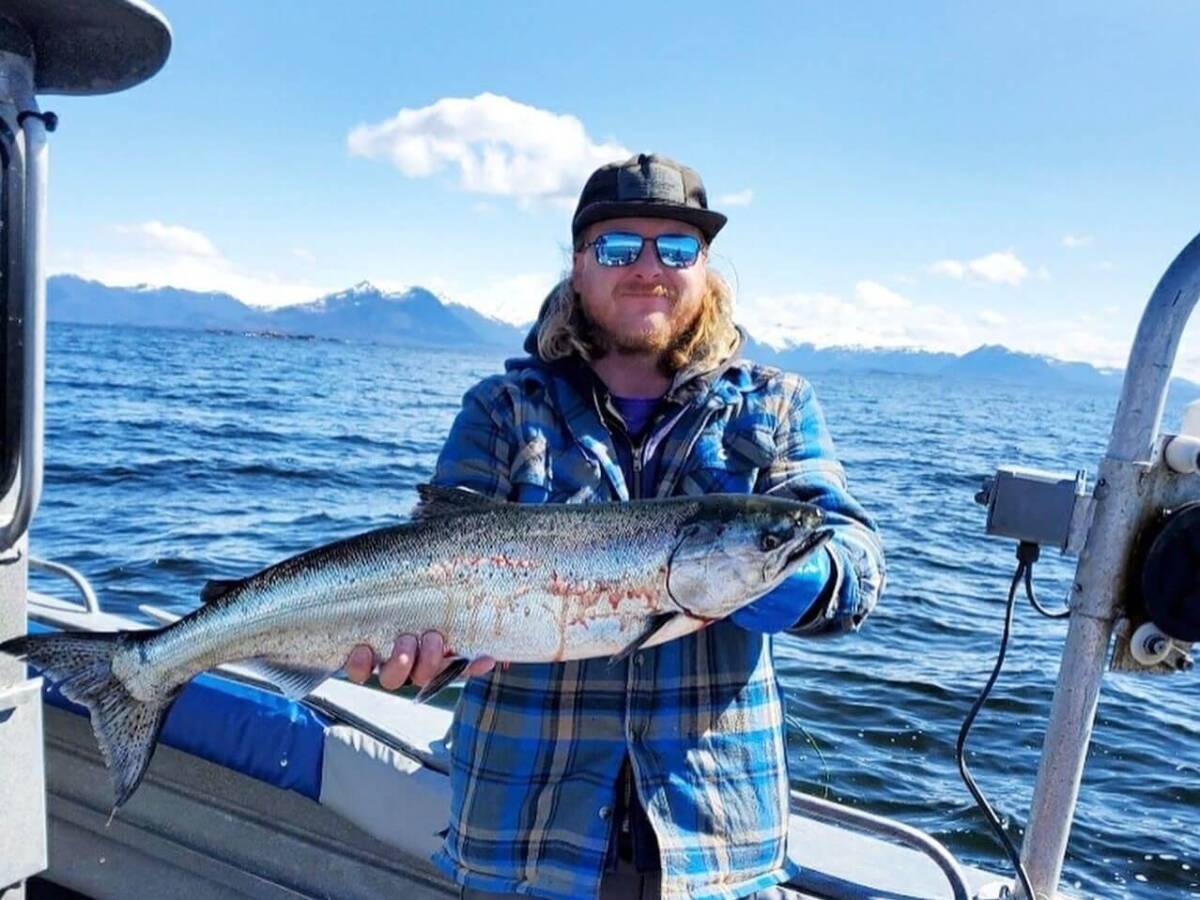 Man in sunglasses holds a salmon on a boat in Sitka, Alaska