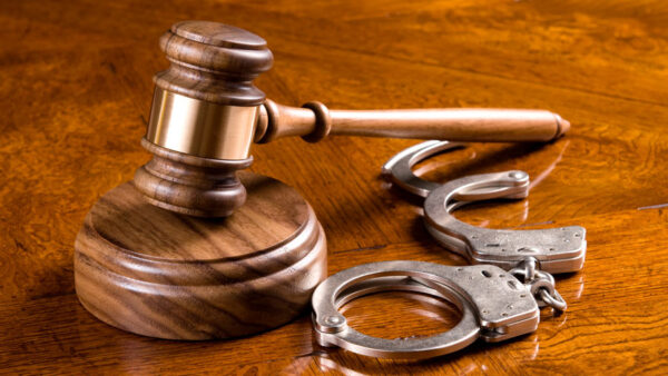 A gavel and block on a rich, cherry desktop with handcuffs.