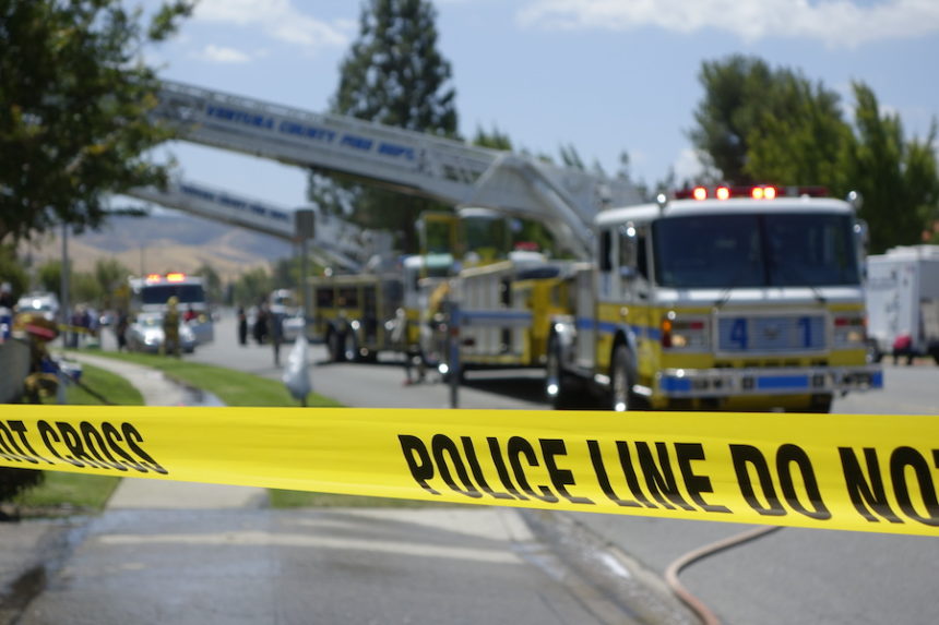 Firemen, Firetrucks and ladders extinguishing a fire behind police barricade caution tape