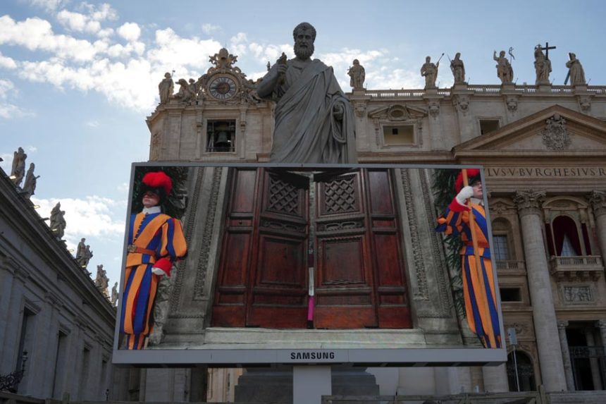 A giant screen in St Peter's Basilica shows a Vatican official closing the door to the Sistine Chapel after calling out "extra omnes", Latin for "all out", during the cardinals' conclave to elect a new pope, at the Vatican, Wednesday, May 7, 2025. | Alessandra Tarantino, Associated Press
