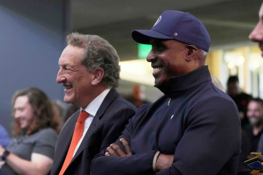 San Francisco Giants President & Chief Executive Officer Larry Baer, left, and former player Barry Bonds listen as Rafael Devers speaks at a news conference before a baseball game between the Giants and the Cleveland Guardians in San Francisco, Tuesday, June 17, 2025. (AP Photo/Jeff Chiu)