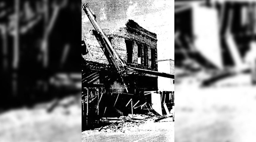 A Murdoch and Walker Concrete pumper arm is shoved against the outside, second story wall of the Dietrich Building to keep it from collapsing onto West Center Street (Pocatello). Long Construction of American Falls Monday started demolishing the downtown landmark which was gutted by an arson-caused fire last January. Other workers have already salvaged whatever they could from the edifice. Caption dated July 26, 1977.