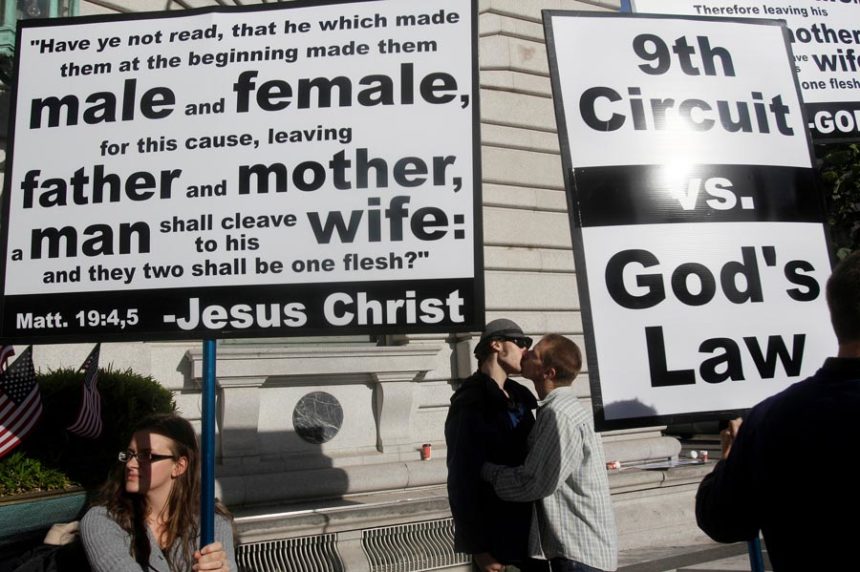 Aiden Lougee, center left, kisses his boyfriend, Rex Resa, seen between signs held by opponents to gay marriage outside of the courthouse after a hearing in the Ninth Circuit Court of Appeals, Monday, Dec. 6, 2010, in San Francisco. | Jeff Chiu, Associated Press