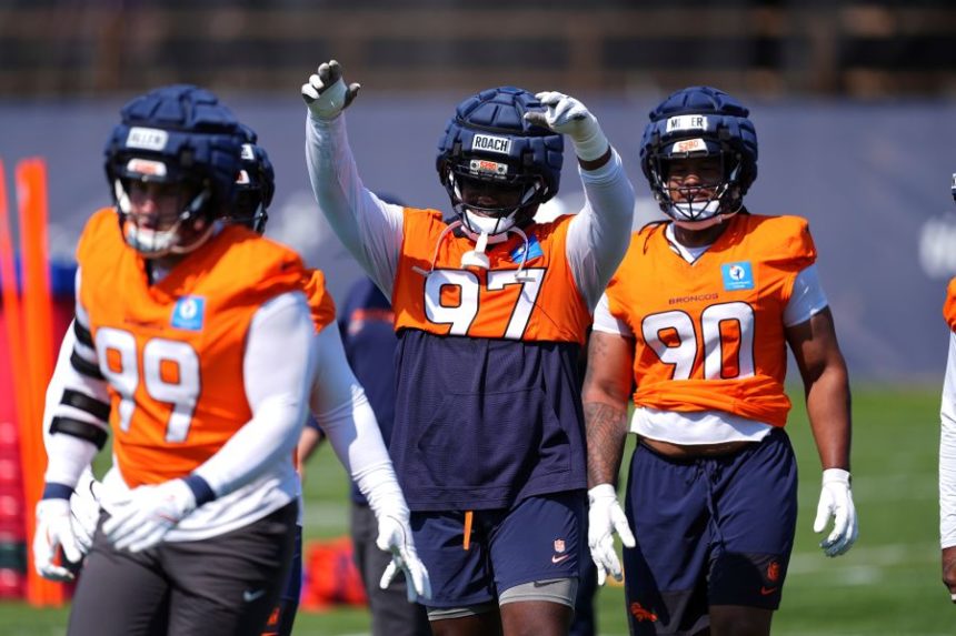Denver Broncos defensive tackle Malcolm Roach, center, raises his arms to acknowledge the applause of fans while warming up between defensive end Zach Allen, front, and defensive tackle Jordan Miller during an NFL football practice Friday, July 25, 2025, in Centennial, Colo. (AP Photo/David Zalubowski)