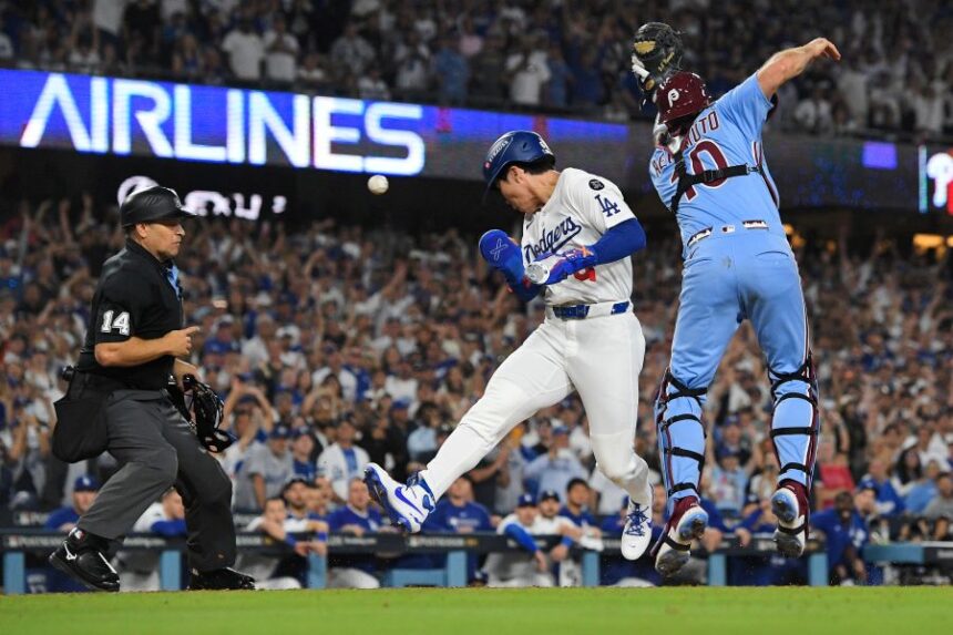 Los Angeles Dodgers' Hyeseong Kim, center, scores the game-winning run past Philadelphia Phillies catcher J.T. Realmuto (10) on a ground ball by Andy Pages and a throwing error by Phillies pitcher Orion Kerkering during the eleventh inning in Game 4 of baseball's National League Division Series Thursday, Oct. 9, 2025, in Los Angeles. (AP Photo/Mark J. Terrill)