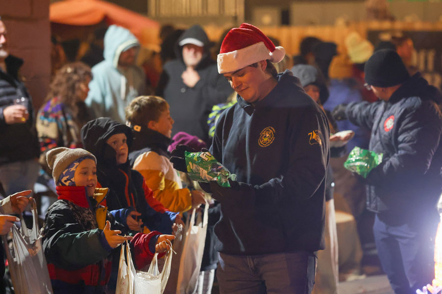  A parade volunteer , bringing holiday cheer to bundled up spectators along the route hands out candy to excited children during the  2025 Christmas Night Lights Parade. 