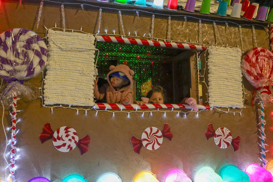 Children look out the window of a homemade gingerbread house float as it makes its way through the  2025 Christmas Night Lights Parade.   