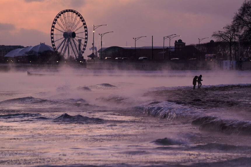 People walk on an ice covered beach along the shore of Lake Michigan, Friday, Jan. 23, 2026, in Chicago. (AP Photo/Kiichiro Sato)