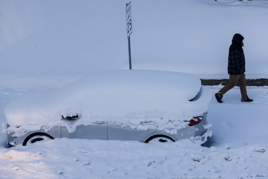 A person walks by a vehicle that was plowed in by snow in Grand Rapids, Mich., on Friday. | Joel Bissell, Kalamazoo Gazette via AP