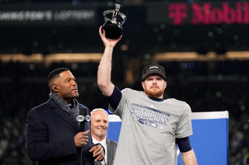 Seattle Seahawks quarterback Sam Darnold lifts the winner's trophy next to Michael Strahan, left, after a win over the Los Angeles Rams in the NFC Championship NFL football game Sunday, Jan. 25, 2026, in Seattle. (AP Photo/Godofredo A. Vásquez)