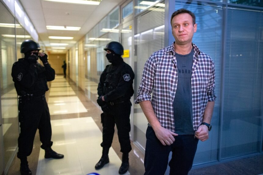 Russian opposition leader Alexei Navalny speaks to the media in front of security officers standing guard at the Foundation for Fighting Corruption office in Moscow, Russia, Thursday, Dec. 26, 2019.