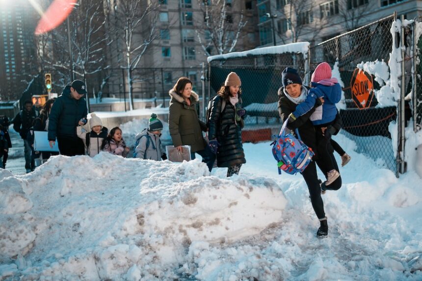 A woman carries a child over piles of plowed snow as she walks a girl to school, Tuesday, Feb. 24, 2026, in New York.