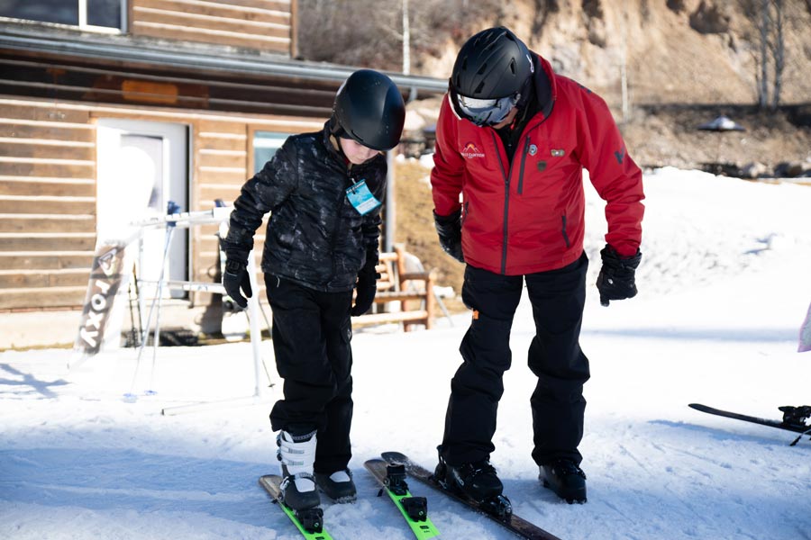 Bob Carlson helps guide Greyson Ward, who is new to skiing, to put on his skis at Kelly Canyon on Friday. | Cody Roberts, EastIdahoNews.com