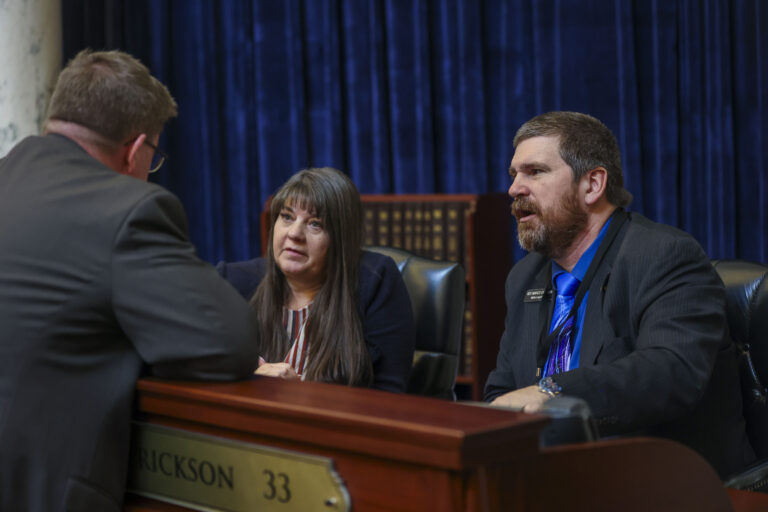 Reps. Tanya Burgoyne, R-Pocatello, and Marco Erickson, R-Idaho Falls, chat with a colleague on the House floor on Jan. 12, 2026, at the State Capitol Building in Boise. (Photo by Pat Sutphin for the Idaho Capital Sun)