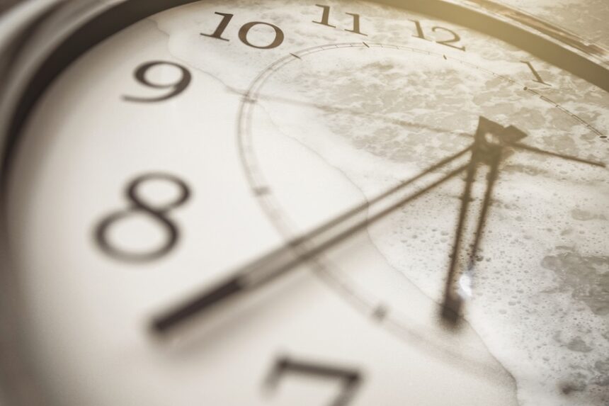 Concept of time and memories. Close-up of the clock and sea wave on the sand.