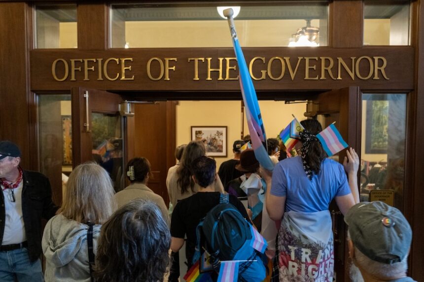 Protestors walk into the entry room to Gov. Brad Little’s office on Wednesday, April 1, 2026, urging him to veto House Bill 822. The bill would require doctors and teachers to out trans kids to their parents, or face lawsuits.