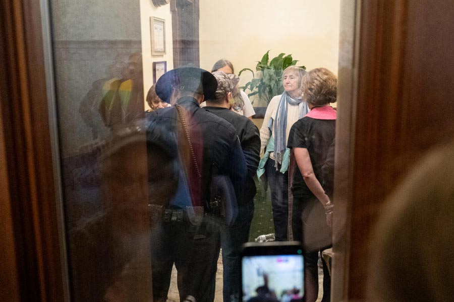 An Idaho State Police trooper handcuffs Nikson Mathews, a trans activist, in the Idaho governor’s office. To the right, the Rev. Sara LaWall is handcuffed on Wednesday, April 1, 2026. | Kyle Pfannenstiel, Idaho Capital Sun