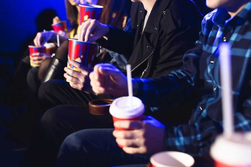 Glasses with a tube and popcorn in the hands of people in a movie theater close-up.