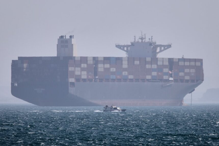 A container ship sits at anchor as a small motorboat passes in the foreground in the Strait of Hormuz off Bandar Abbas, Iran, Saturday, May 2, 2026.
