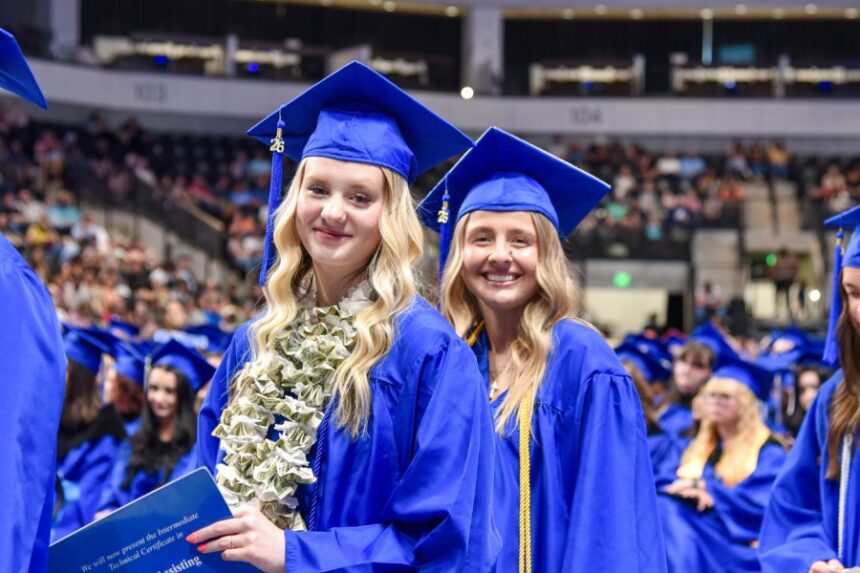 Two female students in blue graduation gowns with crowd in the background. | Courtesy of Brenna N Pincock