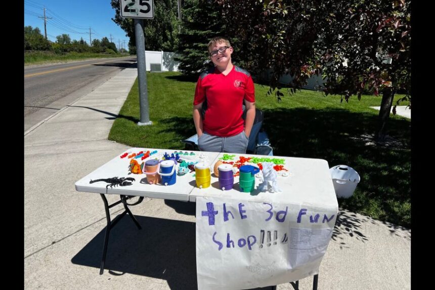Donovan Coon outside with his 3D figure selling stand called the 3d fun shop with an array of various colored, plastic figurines on a table while he smiles. | Courtesy Facebook photo.