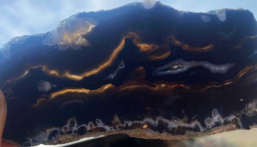 The Teton Range as found in a piece of black agate, Mount Moran on the left followed by a rising sun to its right, the Grand Teton, Middle Teton and the South Teton on the right.