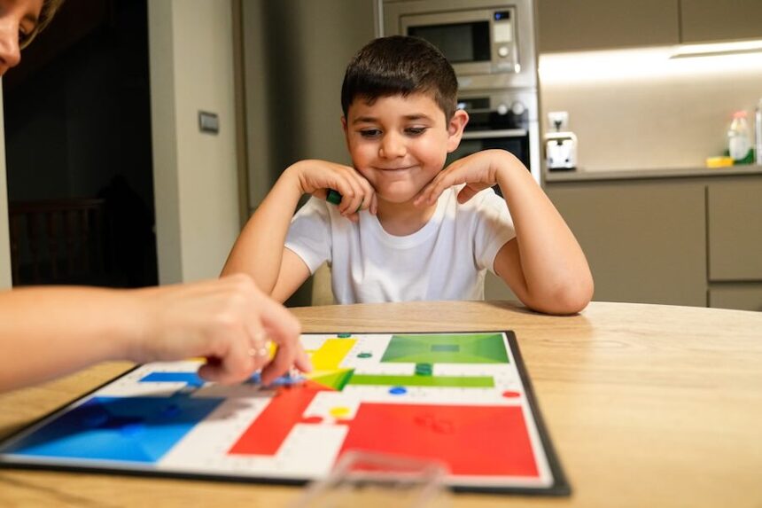 A young boy, smiling and engaged, watches as an adult makes a move in a colorful board game. Concept of family bonding and fun at home. Mentor