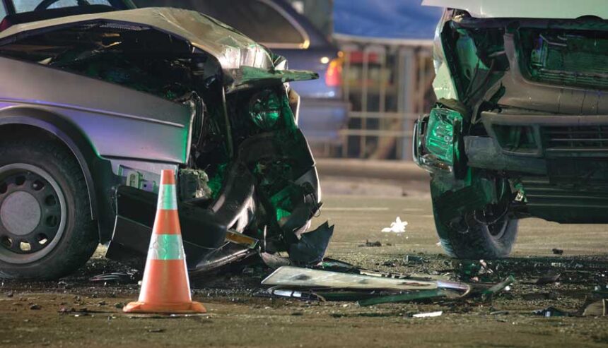 Damaged in heavy car accident vehicles after collision on city street crash site at night.