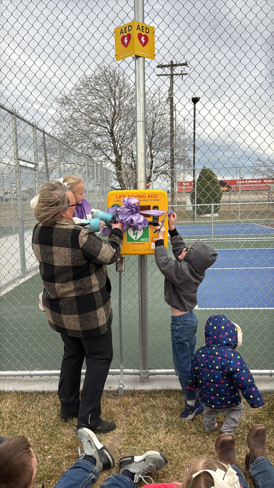 Janelle Palmer's children help cut the ribbon around the AED device.