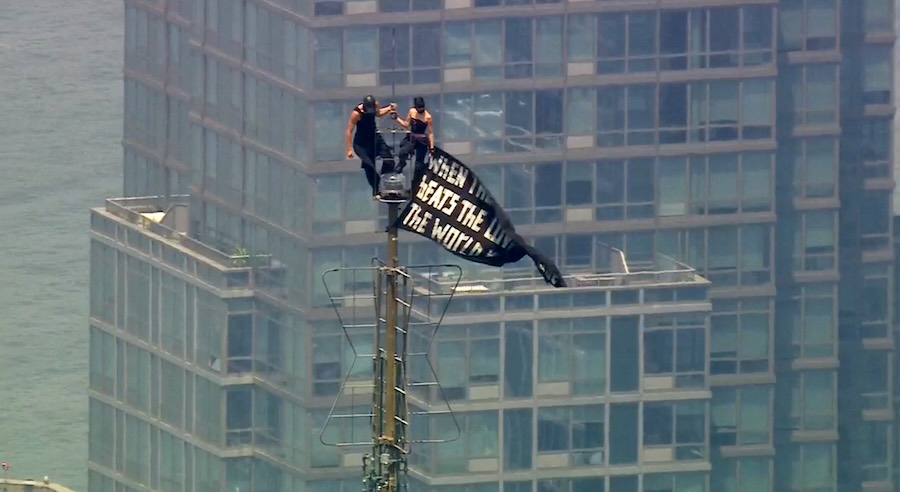 Two people stand on the tip of the antenna of the Empire State Building in New York while holding a banner on Wednesday, July 1, 2026. (WABC-TV via AP) Screenshot