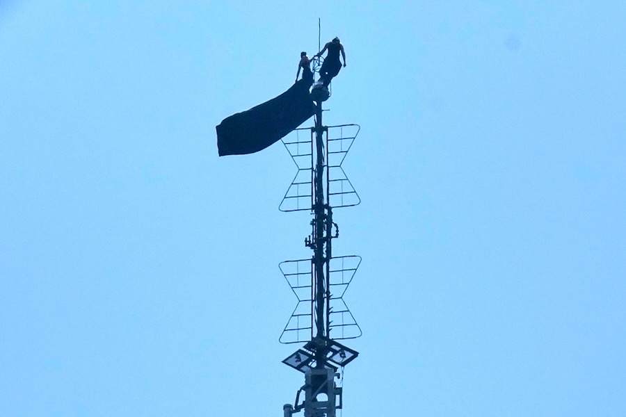Two people stand on the tip of the antenna of the Empire State Building while holding a banner on Wednesday, July 1, 2026.
