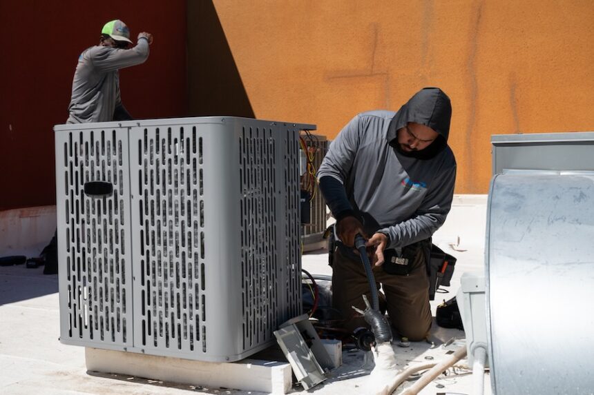 Sonel Telemaque, left, wipes sweat from his brow while installing a new air conditioning unit alongside Brian Hermosillo during record-breaking heat March 19, 2026, in Tempe, Ariz.
