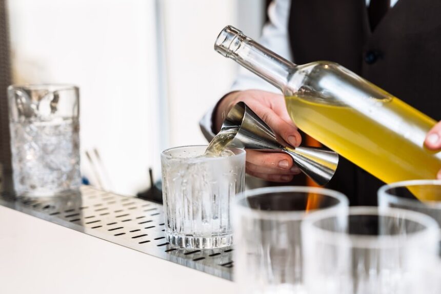 A bartender skillfully pours a colorful cocktail into a glass.