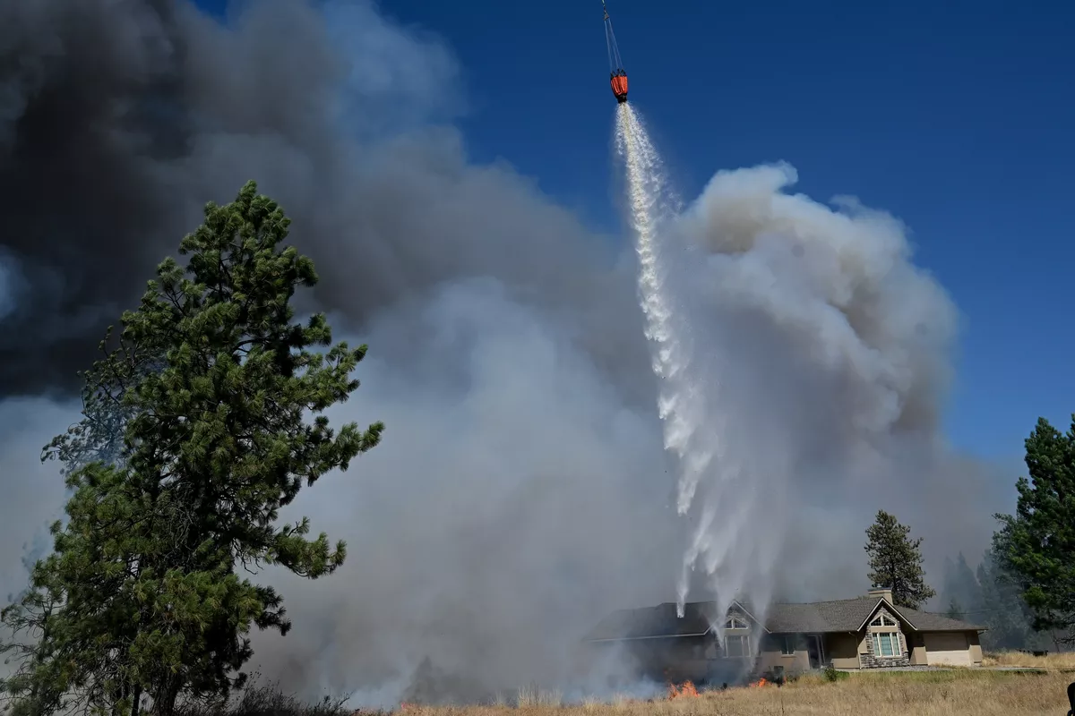 A water drop from a helicopter knocks back flames from the Old Trails fire from a home on Euclid on Saturday, Aug 1, 2026, in Spokane, Wash. (Tyler Tjomsland/The Spokesman-Review)