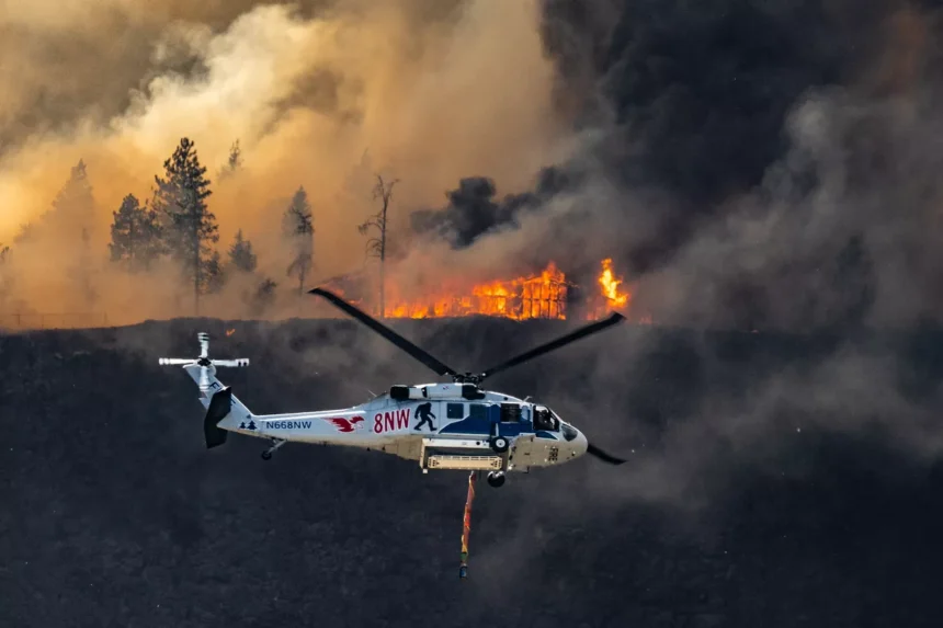 The Old Trails Fire consumes a structure on the ridge above North Aubrey L. White Parkway as a firefighting helicopter heads to the Spokane River for water, Sat. Aug 1, 2026. (COLIN MULVANY/THE SPOKESMAN-REVIEW)