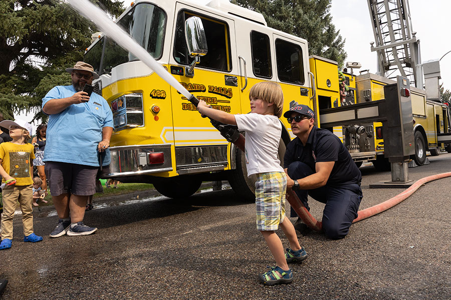 Idaho Falls Firefighter Isaac Snarr helping local children to play with a fire hose, that helped cool off residents during the hot weather at the 35th annual Duck Race. | Daniel V. Ramirez, EastIdahoNews.com