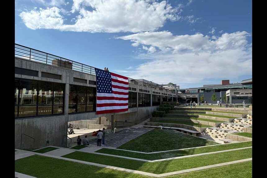 FILE - People gaze down at the site where Charlie Kirk was shot, above which hangs an American flag, at Utah Valley University, Sept. 15, 2025, in Orem, Utah. (AP Photo/Jesse Bedayn, File)